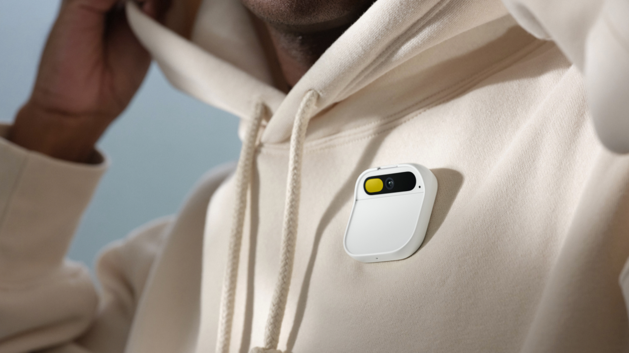 A white Humane Ai pin, worn by a person in a white hoodie.