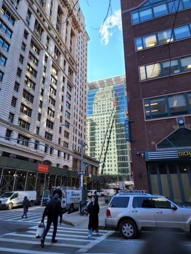 A Manhattan street scene showing a pedestrian on a crosswalk, buildings, and cars.