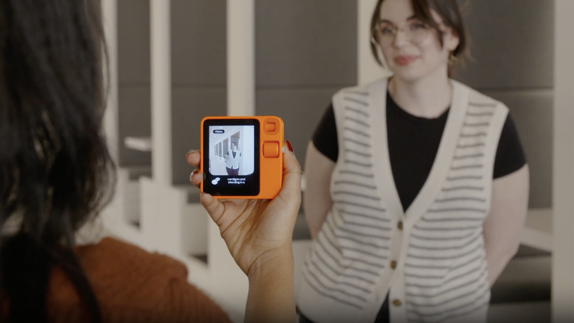 A woman holding the Rabbit r1, using its camera to look at another woman.